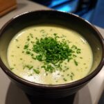 Close-up of creamy, pale green leek soup garnished generously with freshly chopped chives in a dark bowl.