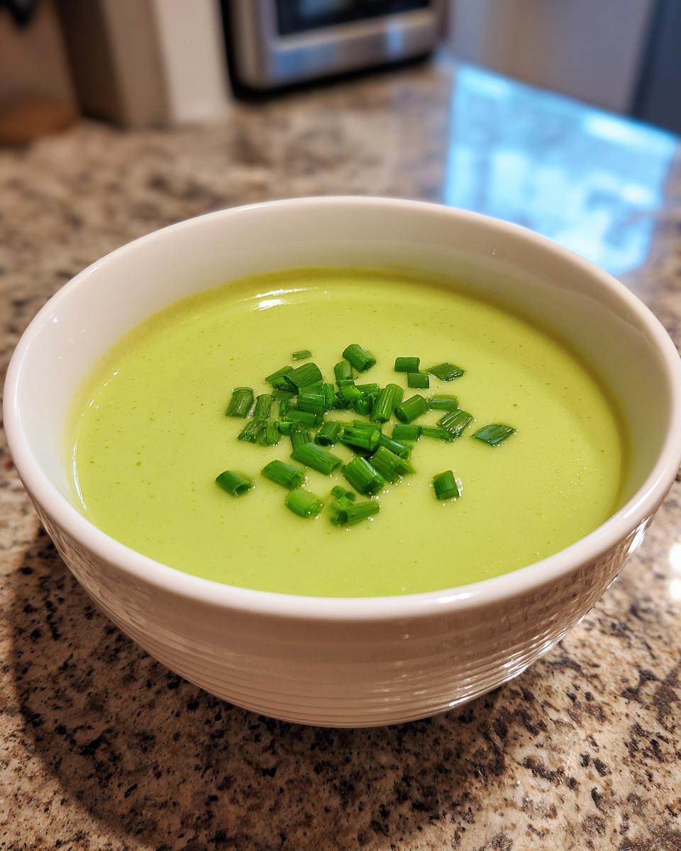 A bowl of vibrant green, creamy leek soup garnished with freshly chopped chives.
