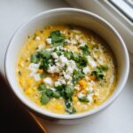 A close-up of creamy Mexican street corn soup topped with cotija cheese, fresh cilantro, and black pepper.