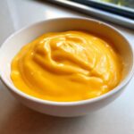 Close-up of thick, bright orange nacho cheese sauce swirled in a small white bowl.