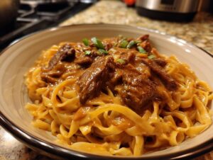 Close-up of fettuccine noodles coated in creamy peanut sauce and topped with savory beef chunks and green onions.