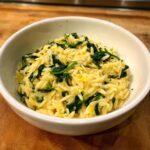 Close-up of creamy orzo pasta mixed with wilted spinach served in a white bowl.