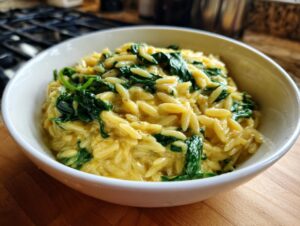 Close-up of creamy orzo pasta mixed with wilted spinach served in a white bowl.