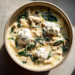Overhead view of a bowl of creamy white chicken lasagna soup topped with dollops of ricotta, spinach, and red pepper flakes.