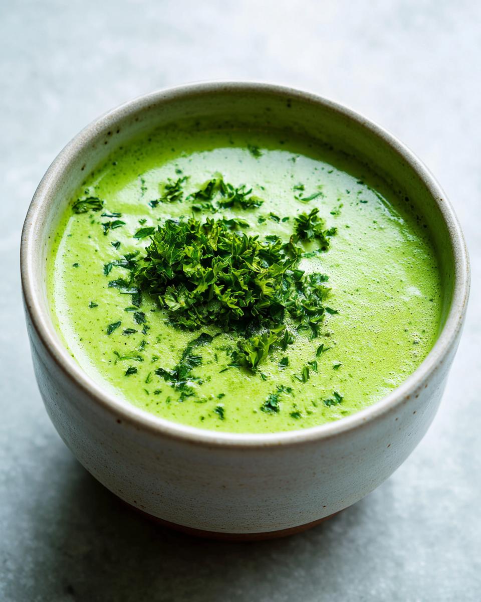 Close-up of a bowl of vibrant green, creamy zucchini soup garnished with fresh chopped parsley.