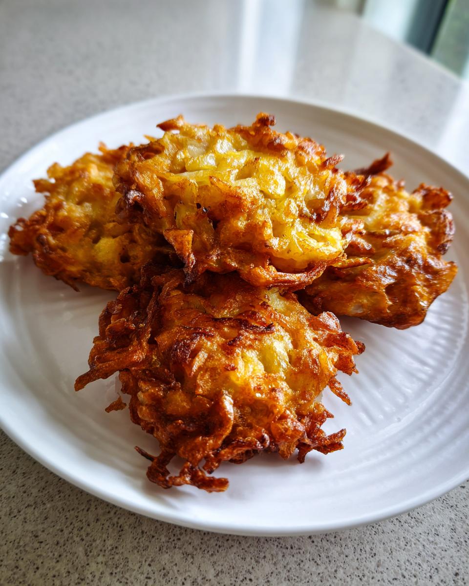 Four golden-brown, crispy Amish Onion Fritters piled on a white plate.