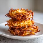 A stack of three golden-brown, crispy Amish Onion Fritters piled on a white plate.