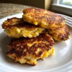A stack of four golden-brown, crispy corn fritters showing visible kernels of corn inside.