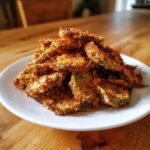 A close-up of a tall pile of golden brown, crispy Fried Pickles served on a white plate.
