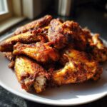 A pile of perfectly cooked, crispy, and seasoned chicken wings stacked high on a white plate.