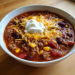 Close-up of a bowl of rich crockpot cowboy soup filled with ground beef, beans, corn, topped with shredded cheese and sour cream.