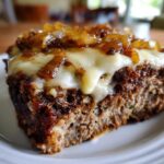Close-up of a slice of crockpot french onion meatloaf topped with melted white cheese and caramelized onions.