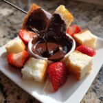 A piece of cake being dipped into rich, melted chocolate fondue, surrounded by fresh strawberries.