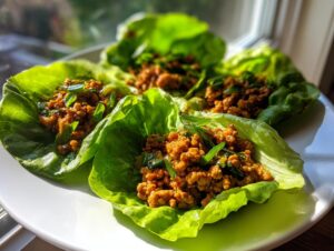 Four bright green lettuce cups filled with savory ground chicken mixture, ready to eat as chicken lettuce wraps.