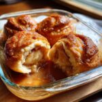 A close-up of warm apple dumpling cut in half showing the soft apple filling, sitting in rich caramel sauce.