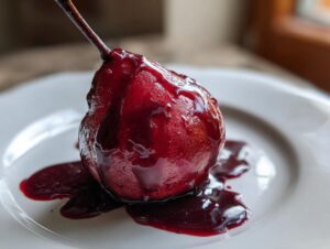 A close-up of a single, deep red poached pears dessert sitting on a white plate, covered in rich syrup.