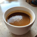 Close-up of a small white cup filled with a rich, dark brown liquid with crema, resembling espresso, not turkey gravy.