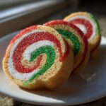 Three slices of colorful pinwheel cookies featuring red, white, and green swirls, coated in sparkling sugar.