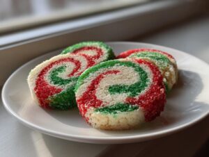 Four slices of festive red, green, and white pinwheel cookies coated in sparkling sugar on a white plate.