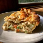 A close-up of a slice of turkey pot pie showing flaky golden crust and creamy filling with shredded turkey and vegetables.