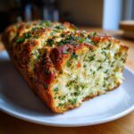 A freshly baked, golden brown loaf of garlic herb bread, rich with parsley, served on a white plate.
