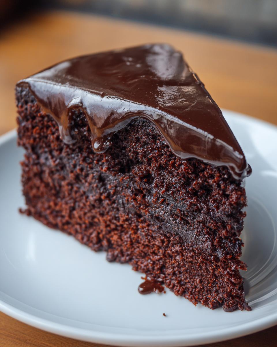 Close-up of a moist slice of flourless chocolate cake topped with glossy chocolate ganache.