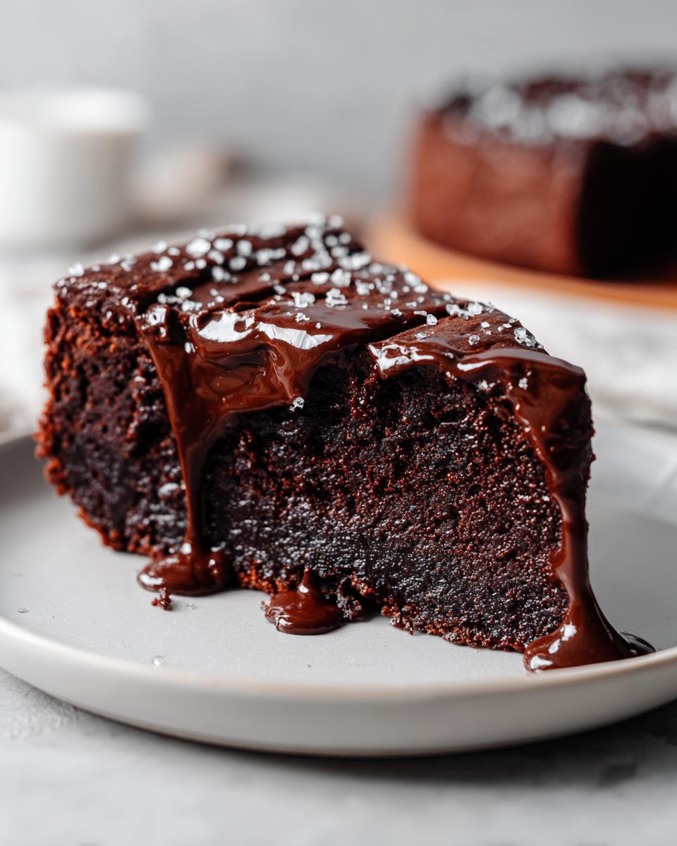 A decadent slice of flourless chocolate cake topped with glossy chocolate ganache and sea salt flakes.