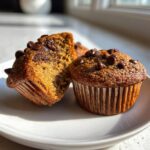 Two delicious banana chocolate chip muffins, one whole and one cut in half showing the moist interior.