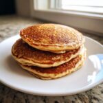 A tall stack of three golden-brown, fluffy banana pancakes resting on a white plate.