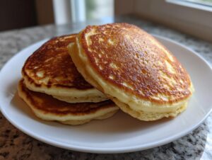 A stack of three golden-brown, fluffy banana pancakes served on a white plate.