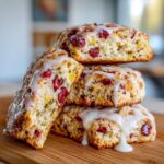 A stack of three fluffy cranberry orange scones drizzled generously with white vanilla glaze.