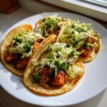 Four freshly made salmon tacos filled with seasoned fish chunks and topped with shredded cabbage slaw.
