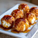 Close-up of six golden-brown, breaded goat cheese balls drizzled with dark honey or syrup.