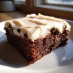 A single, rich square of gingerbread brownies topped with thick, creamy frosting and chocolate chips.