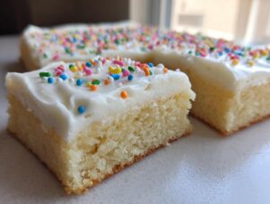A close-up of a square cut of soft, vanilla sugar cookie bars topped with white frosting and colorful sprinkles.