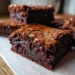 A close-up, low-angle shot of a fudgy brownie piece showing its rich, moist interior and cracked, shiny top.
