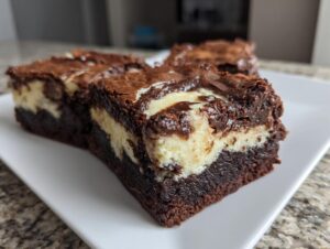 Close-up of fudgy cream cheese brownies with a distinct cream cheese swirl layer, served on a white plate.