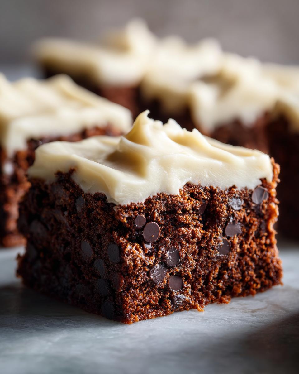 A single square of rich, dark gingerbread brownies studded with chocolate chips and topped with thick cream cheese frosting.