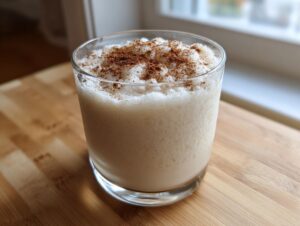 A glass filled with creamy, frothy coquito recipe, dusted generously with ground cinnamon on top.