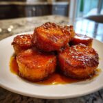 A stack of thick, round southern candied yams glistening with rich, amber glaze on a white plate.