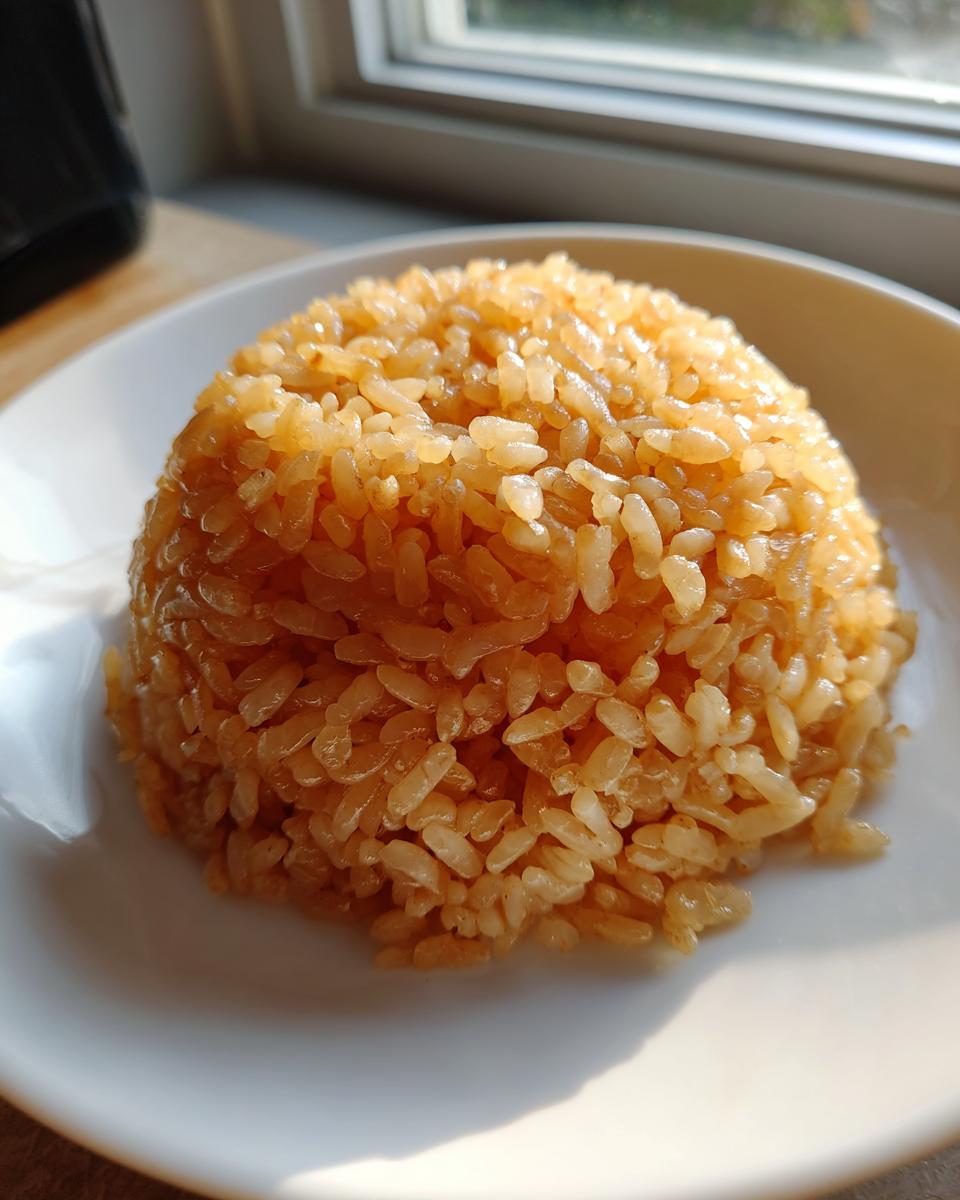 Close-up of perfectly seasoned, glossy sushi rice molded into a mound on a white plate.