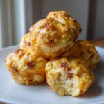 A stack of golden brown, cheesy egg bites, with one showing a fluffy interior and bits of bacon.