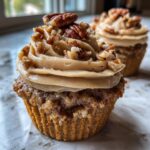 Close-up of a delicious pecan pie cupcake topped with swirled praline frosting and whole/chopped pecans.