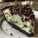 A close-up slice of grasshopper pie showing mint green filling, chocolate layer, and dark chocolate topping.