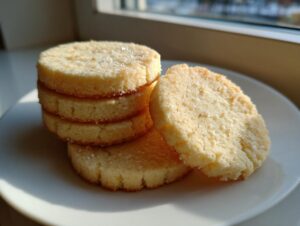 A stack of four golden, round butter cookie slices sprinkled with sugar on a white plate.