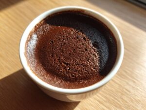 Close-up overhead view of rich, dark homemade chocolate pudding with a slightly textured surface in a white ramekin.