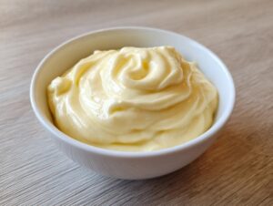 A close-up of thick, pale yellow homemade mayonnaise swirled beautifully in a small white bowl.