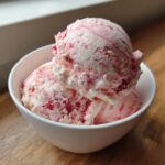Close-up of two scoops of homemade strawberry ice cream with visible berry swirls in a white bowl.