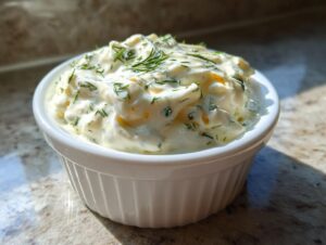 A close-up of creamy, homemade tartar sauce recipe garnished with fresh dill in a small white bowl.