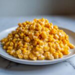 A mound of creamy, golden honey butter corn served on a white plate.